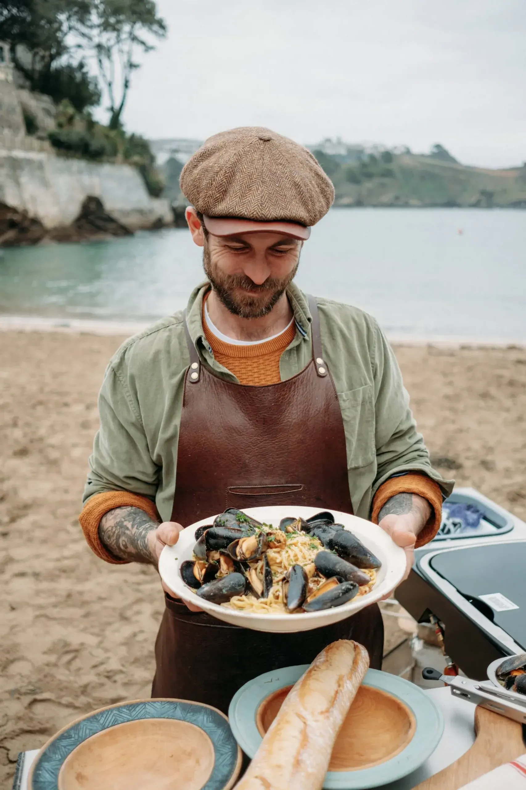 James Strawbridge holding a plate of mussel pasta during an outdoor food production on a Cornish beach