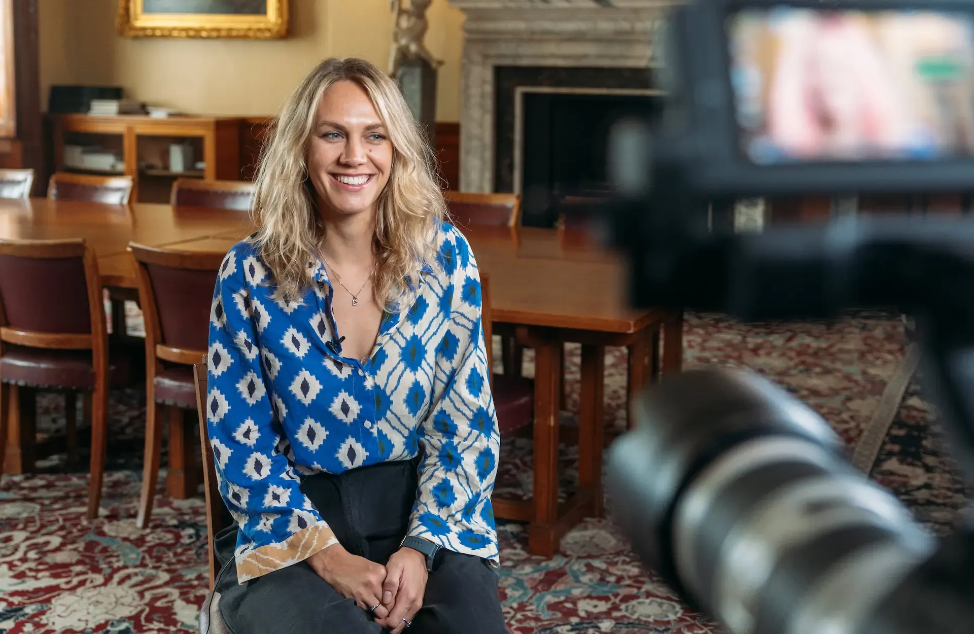 Woman smiling during an on-camera interview for the Marine Stewardship Council UK Awards, with cinema camera in foreground and elegant interior setting behind
