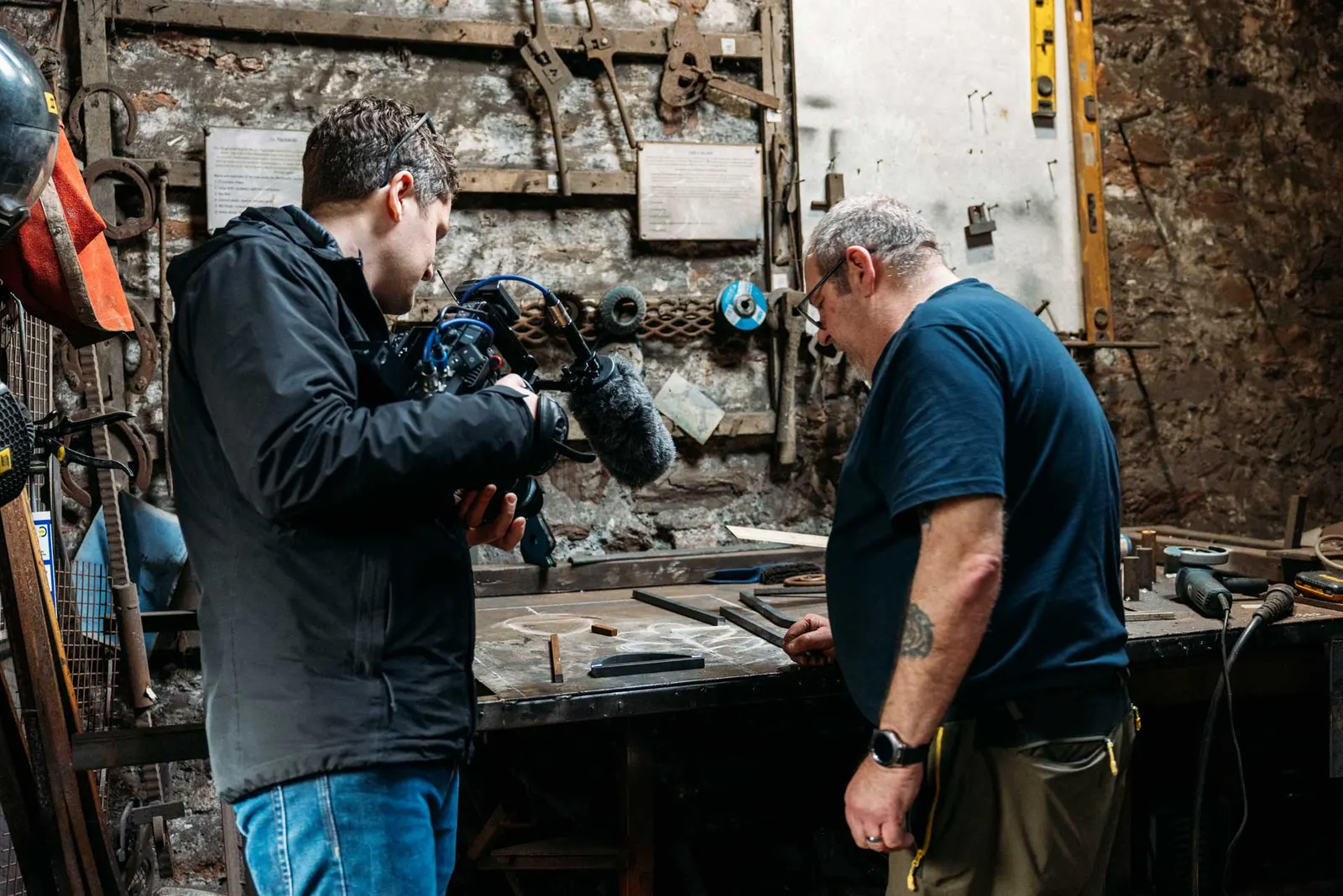 A PixelRain camera operator filming a blacksmith at work inside a traditional workshop